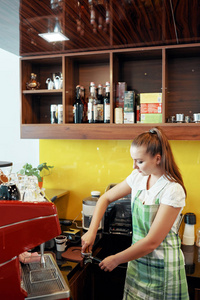 年轻女子穿着绿色围裙，在现代咖啡店的咖啡师的侧景