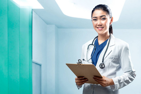 微笑的亚洲女医生，穿着白色外套，拿着剪贴板的听诊器