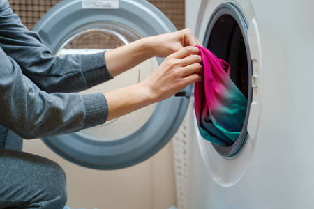 妇女折叠衣服进入洗衣机的照片