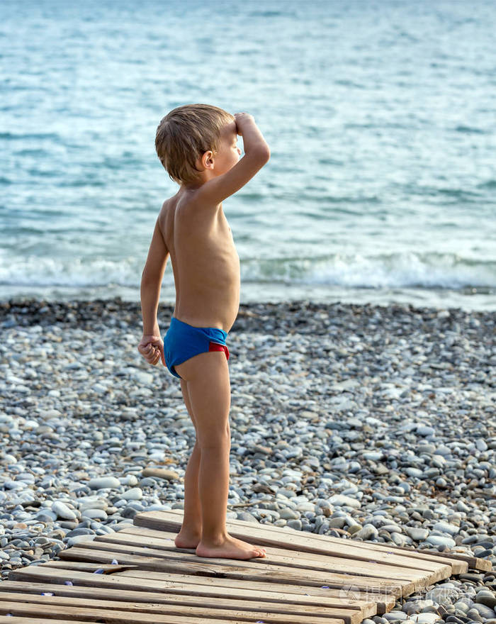 小男孩站在沙滩上,抬起手来望着远处