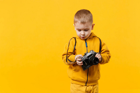 小男孩34岁，穿着黄色衣服，手持相机，孤立在橙色墙上，背景是儿童工作室的肖像。 人们真诚的情感，童年的生活方式概念。 模拟复制空
