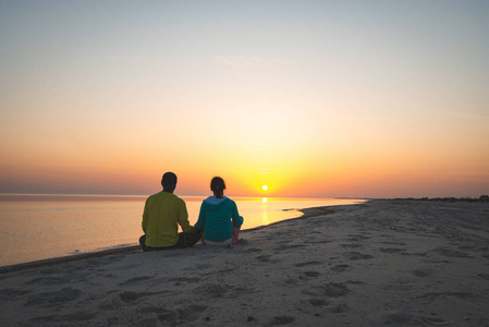 浪漫的一对旅行者坐在海滩上，欣赏大海上的夕阳。 后视图复古图像。