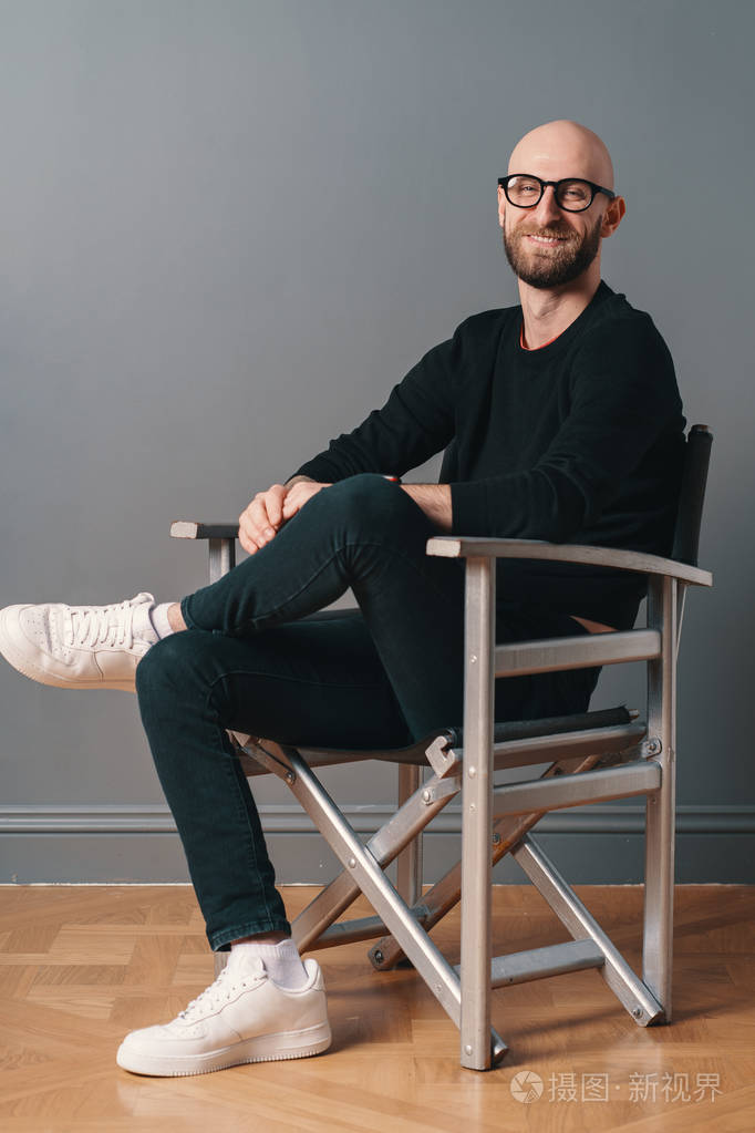 一个现代时尚的男人坐在腿上,在灰色的墙壁背景下,在工作室的一张银色