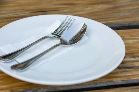木桌上有白色盘子的叉子和勺子