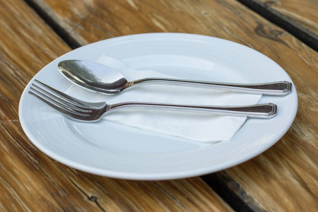 木桌上有白色盘子的叉子和勺子