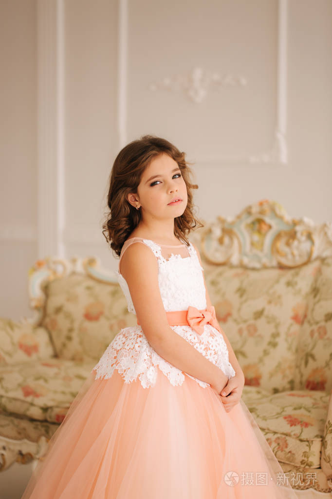 快乐的小公主在美丽的礼服步行通过大工作室