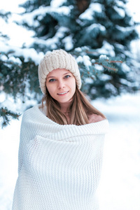 一个女孩的肖像在冬天的森林背景下被白雪覆盖的树木。戴着白色格子和白帽子。美丽的女人在公园里的冬天