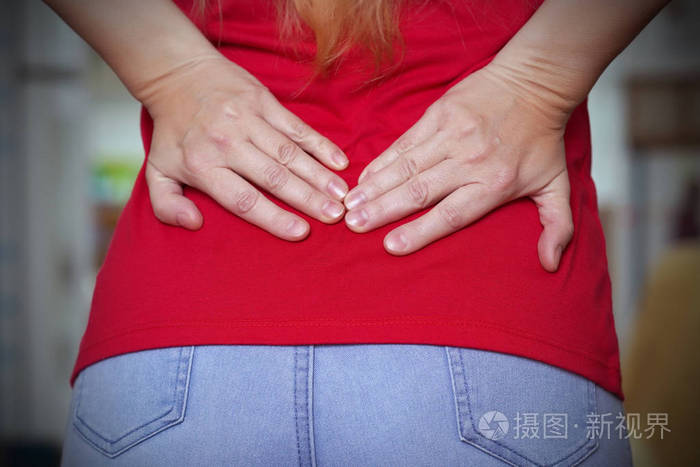 穿蓝色牛仔裤的年轻女人肾脏疼痛背疼的年轻女子把手握在下背部