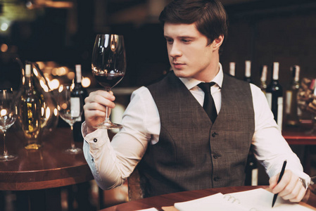 年轻自信的侍酒师在笔记本上做笔记, 在餐厅品尝葡萄酒。品酒
