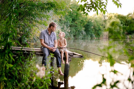爸爸和儿子在湖边钓鱼。 父亲和他的儿子一起钓鱼，从鱼，夏天快乐的童年。