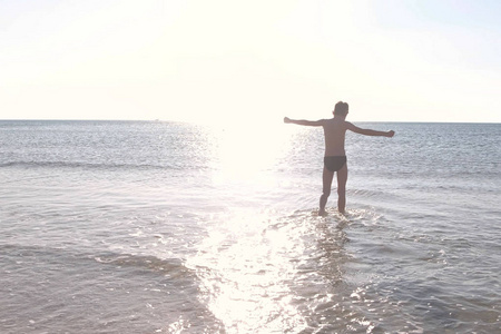 日落时, 男孩的剪影在海水旁散步。在海里游泳