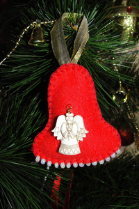 圣诞树上的手工圣诞玩具。 用天使雕像和白色珠子制成的明亮的红色铃铛