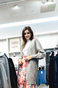 年轻美丽情绪化的现代女性走过购物中心，看着服装店里的时装