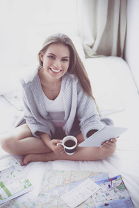 坐在床上的放松的年轻妇女与一杯咖啡和数字式片剂