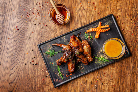 印度美食的概念..用蜂蜜芥末酱烤鸡翅和腿。在餐馆里用黑色盘子端盘子。木制桌子上的印度香料。背景图像。