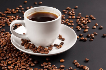 白色杯浓咖啡在烤咖啡豆在坚实的黑色背景前景关闭。
