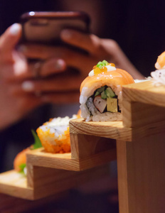 女性使用智能手机拍摄日本新鲜鱼食物鲑鱼寿司卷装饰在传统日本餐厅的木制台阶上。 丰富鱼类营养理念的健康食品