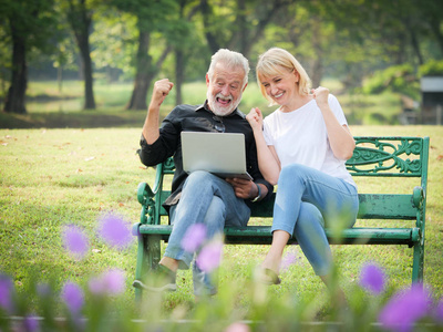 两个快乐的老年人退休，男人和女人坐在公园里使用电脑笔记本电脑