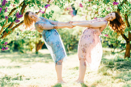 年轻的双胞胎姐妹穿着不同的衣服，在盛开的夏季植物园里玩得开心