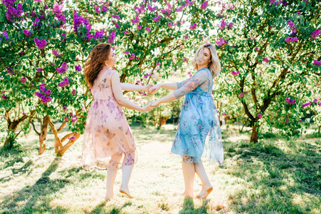 年轻的双胞胎姐妹穿着不同的衣服，在盛开的夏季植物园里玩得开心