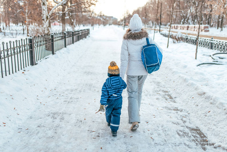 年轻的母亲和她的小男孩儿子手拉手。在冬天在城市在新鲜空气。照顾和照顾孩子的概念, 护送到幼儿园