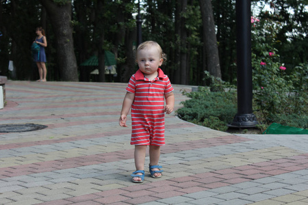 可爱的金发小男孩穿着红色的婴儿套装在公园里散步