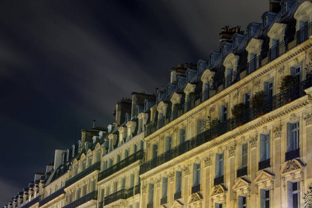 神秘的巴黎住宅建筑古典立面夜间与抽象的黑暗多云的天空。 长期暴露法国