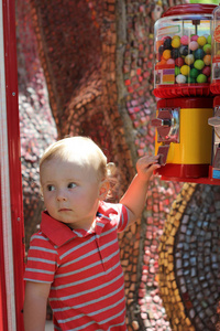 可爱的小男孩站在公园里，靠近五颜六色的装置，穿着红色的婴儿套装。 小孩触摸按钮