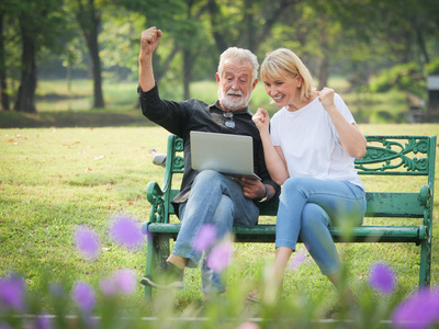 两个快乐的老年人退休了男人和女人坐在公园里使用电脑笔记本电脑