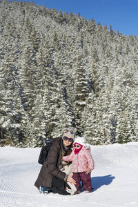 幸福的家庭母亲和孩子女儿有乐趣，拥抱在一个冬天的雪山。育儿概念