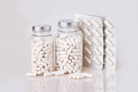 白色软明胶胶囊在透明玻璃瓶与一些分散的桩分离在白色背景.