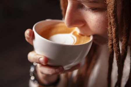 暖冬背景特写一杯白色杯热拿铁艺术咖啡,心形在一个年轻女孩的手中.