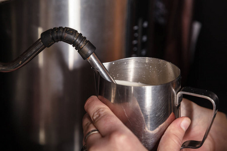 咖啡馆的咖啡师用专业的咖啡机将牛奶倒入金属壶中。咖啡屋的概念。制作卡布奇诺或拿铁的过程