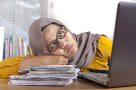 亚洲穆斯林女商人在办公室的笔记本电脑前看着疲惫困倦和懒惰，等待糟糕的互联网连接