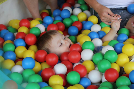 带着婴儿的妈妈在游泳池玩耍，为了好玩，男孩在彩色塑料球里挖洞。