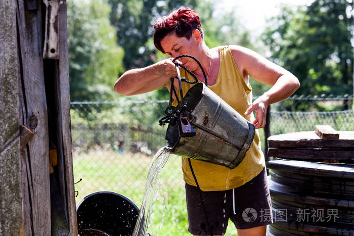中年妇女将水从水桶里倒到一个浅水池里.