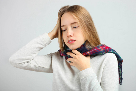 悲伤的白种人女孩戴着围巾在中立的背景下。 头痛喉咙痛。 概念健康。