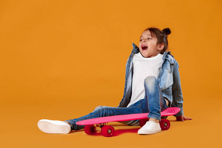 时尚的小女孩与滑板在粗斜纹棉布橙色背景