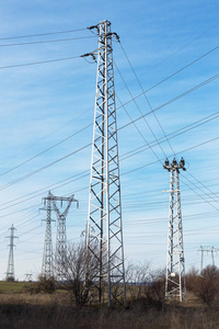 高压线路和电力塔在一个平坦和绿色的农业景观在一个阳光明媚的日子，卷云在蓝天。 塔架和输电线路