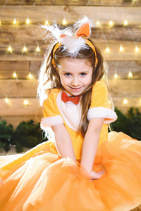 带着微笑的白种人小女孩穿着橙色的裙子在圣诞树上