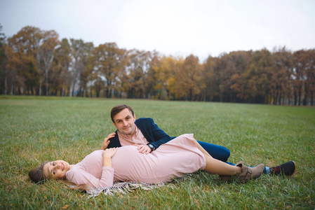 穿着衣服的孕妇，在公园里的爱人，在绿草如茵的草地上寒冷