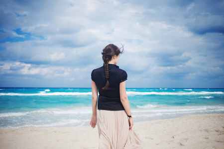 穿着长裙走在海洋上的年轻女子的后视