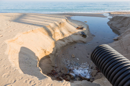工业废水，管道排放液体工业废物到海洋在一个城市海滩。 污浊的污水从塑料污水管流到海滨城市海滩的沙滩上