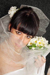 新娘用花束遮住面纱的脸。