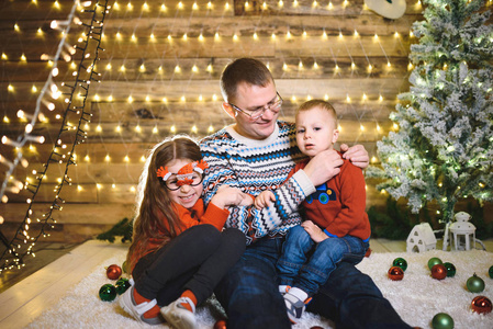 快乐的白种人父亲和孩子们一起在圣诞屋里，有着明亮的花环和装饰的树