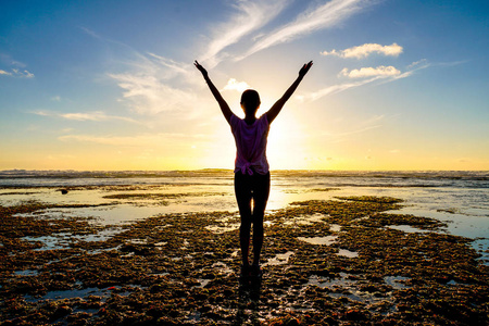在海边夕阳下坚强的自信女人. 年轻女人在海滩上做瑜伽的剪影.掌