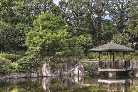 美次郎花园中央池塘里的六角形露台，鲤鱼在那里游泳，周围是日本松树的叶子下的巨大的扁平石头，还有各种像伊罗哈莫米吉亚马莫米吉