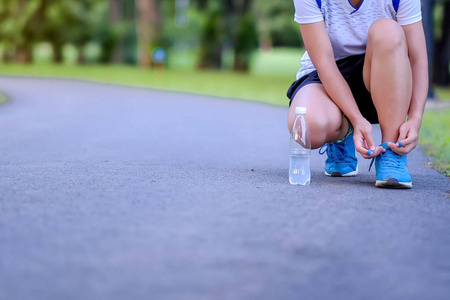年轻的运动员女士在公园里系跑鞋，户外女跑步者准备在亚洲以外的道路上慢跑，早上在人行道上散步和锻炼。 健康和体育概念