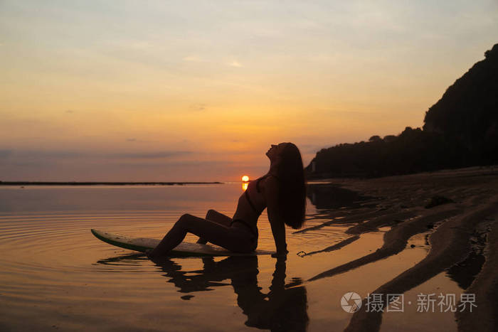 照片 人物 在美丽的日落背景下, 在海边的冲浪板上坐着的女孩的剪影和