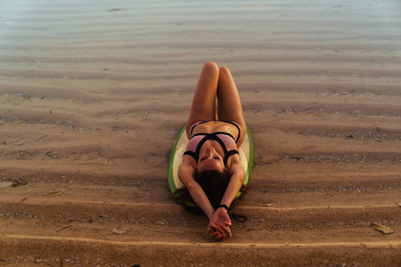 穿着泳衣的冲浪者女孩躺在海边的冲浪板上